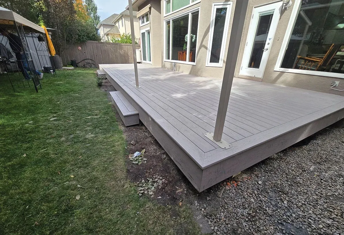 Newly installed wooden deck adjacent to a green lawn and gravel.